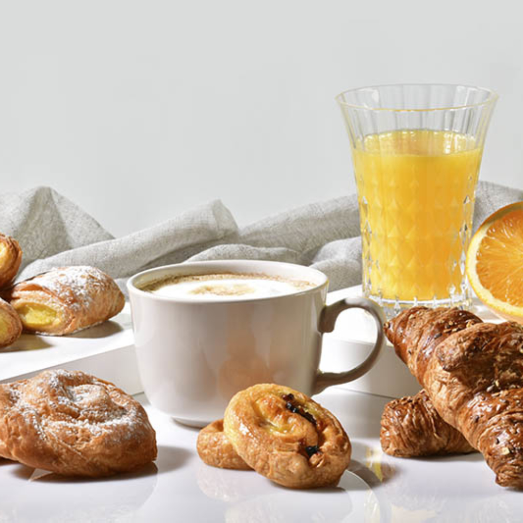 Cup of coffee surrounded by delicious pastries, with an orange juice and half orange at the back on a light background. Traditional breakfast concept.