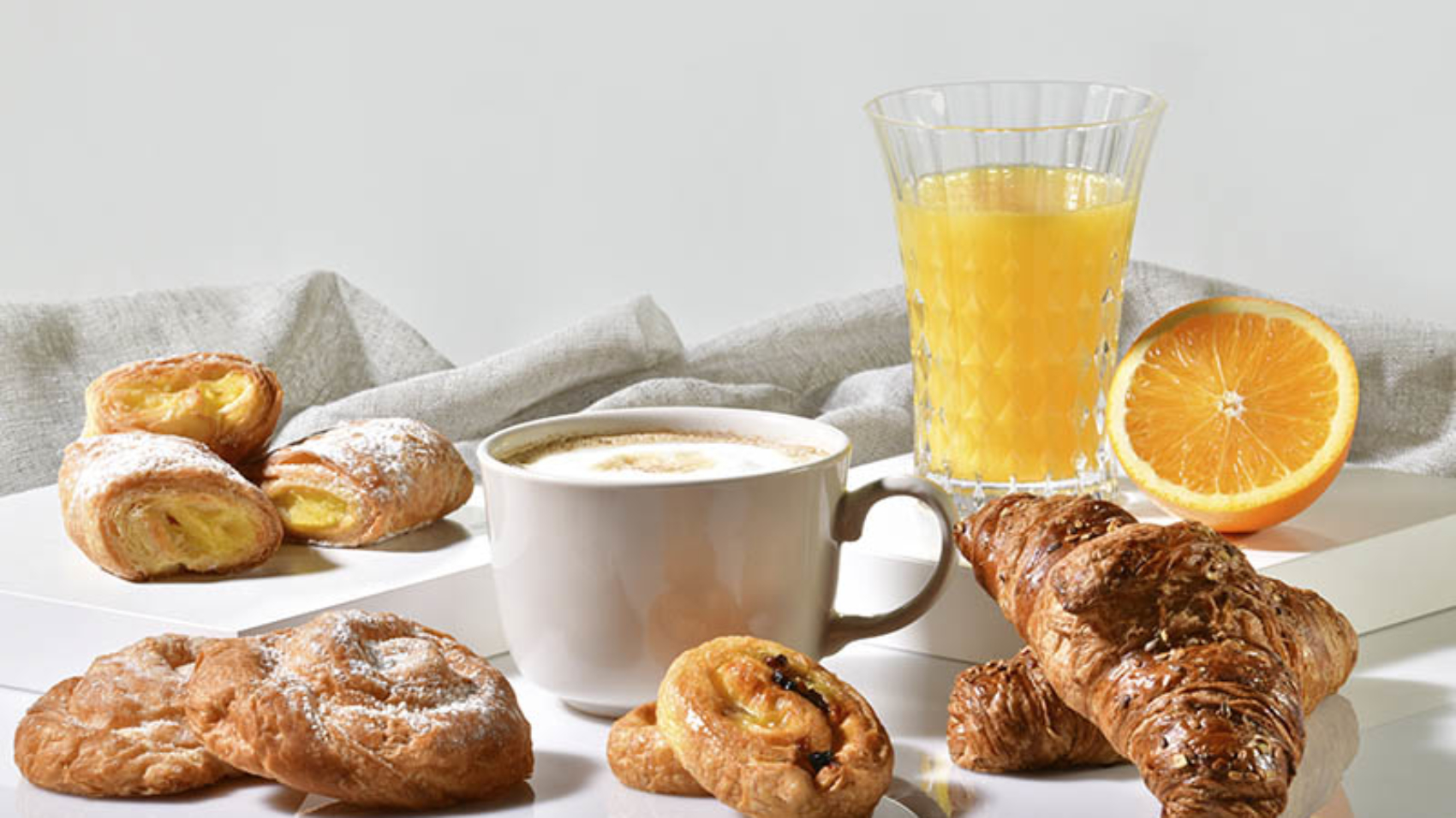 Cup of coffee surrounded by delicious pastries, with an orange juice and half orange at the back on a light background. Traditional breakfast concept.